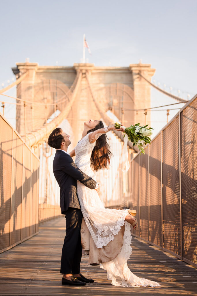 Couple in formal engagement attire on the Brooklyn Bridge at sunrise, featuring a flowing lace gown and tailored navy suit, exemplifying what to wear for engagement photos in DUMBO with structured silhouettes, romantic movement, and iconic architectural backdrop NYC symmetry.