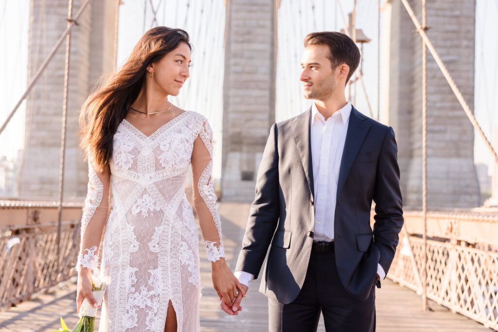 Couple walking hand in hand on the Brooklyn Bridge during sunrise, illustrating why early morning is the Best time for a DUMBO engagement session.