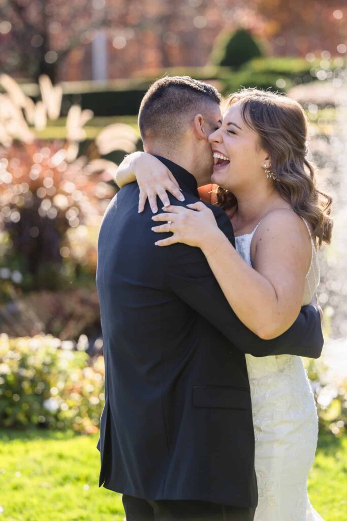 Joyful bride embracing her groom during their first look at a Vineyard at East Wind wedding, surrounded by golden sunlight and lush fall landscaping.