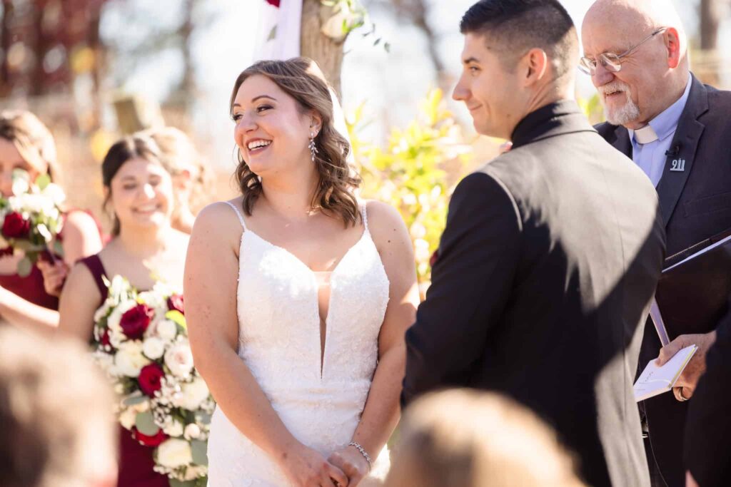 Bride smiling joyfully during outdoor ceremony at the Vineyard at East Wind wedding, with groom and officiant under sunny skies in Long Island’s vineyard setting.