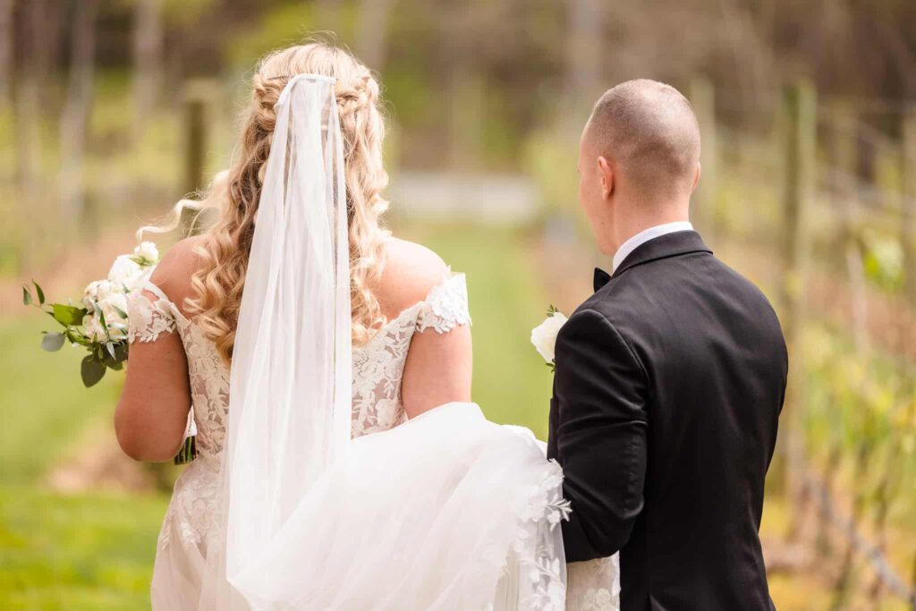 Bride and groom walk hand in hand through vineyard rows, showcasing the romantic outdoor setting in Long Island.