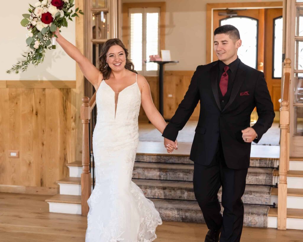 Bride and groom making a joyful grand entrance into their Vineyard at East Wind wedding reception, with bride raising bouquet in celebration.
