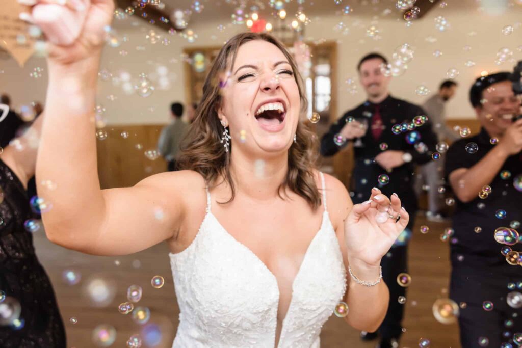 Bride laughing and dancing joyfully among bubbles during lively Vineyard wedding reception celebration.