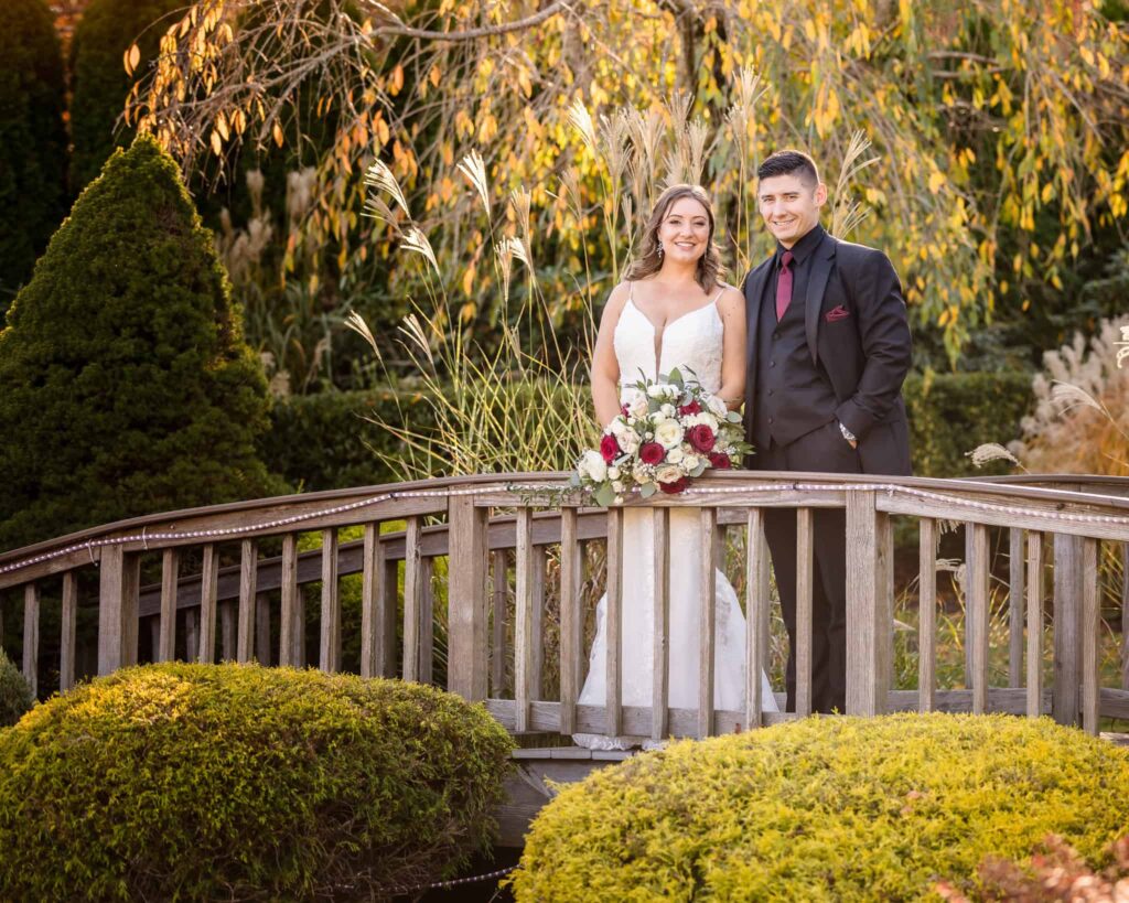 Bride and groom posing on a wooden bridge surrounded by fall foliage at the Vineyard at East Wind on their wedding day.