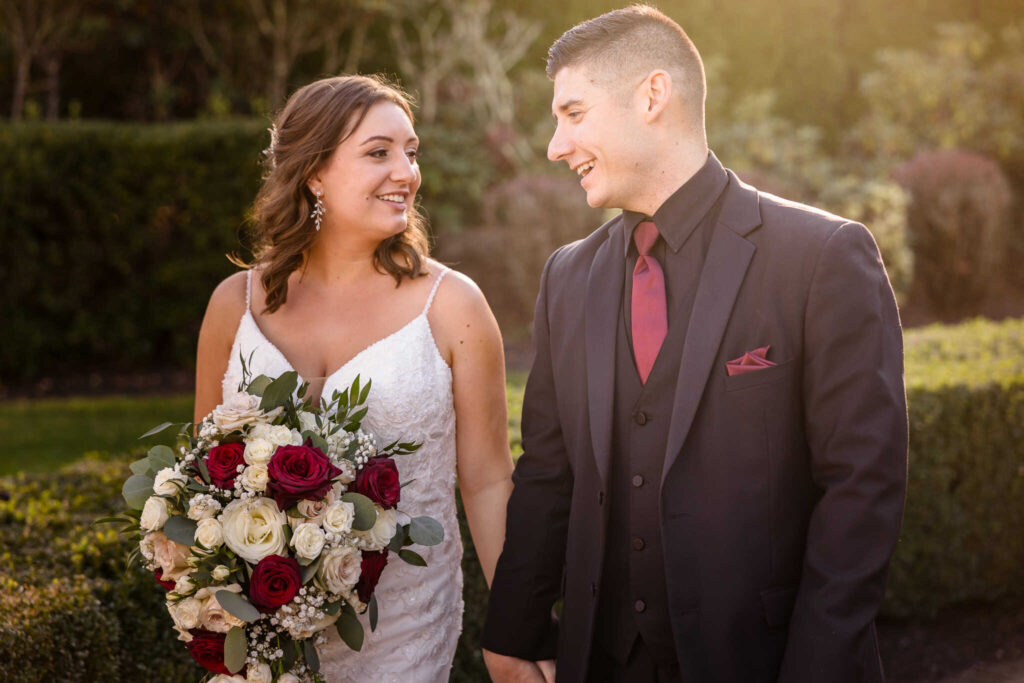Bride and groom smiling at each other while holding hands during golden hour at the Vineyard at East Wind.