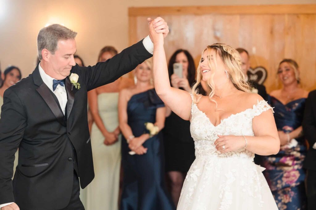 Bride sharing a joyful father-daughter dance at her wedding reception, surrounded by smiling guests.