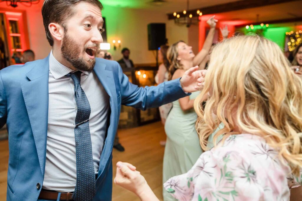 Wedding guests dancing and celebrating on the reception floor with colorful lighting.