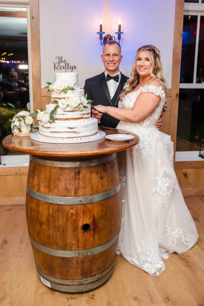 Bride and groom smiling as they cut their white semi-naked wedding cake decorated with roses.
