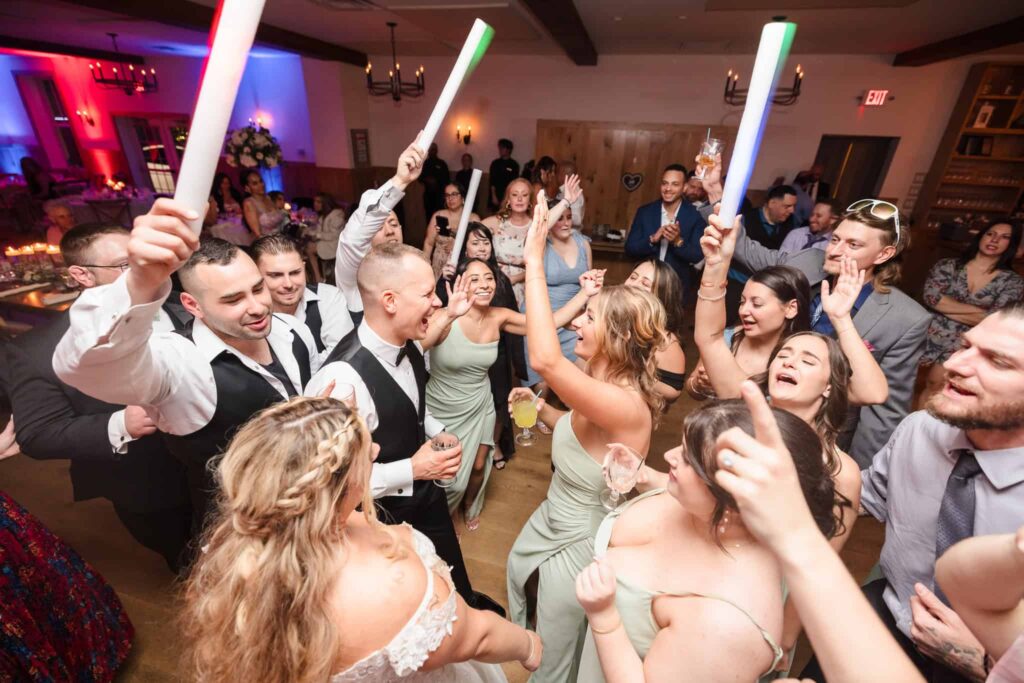Wedding guests and newlyweds dancing and celebrating with glow sticks during a lively reception at the Vineyard at East Wind.
