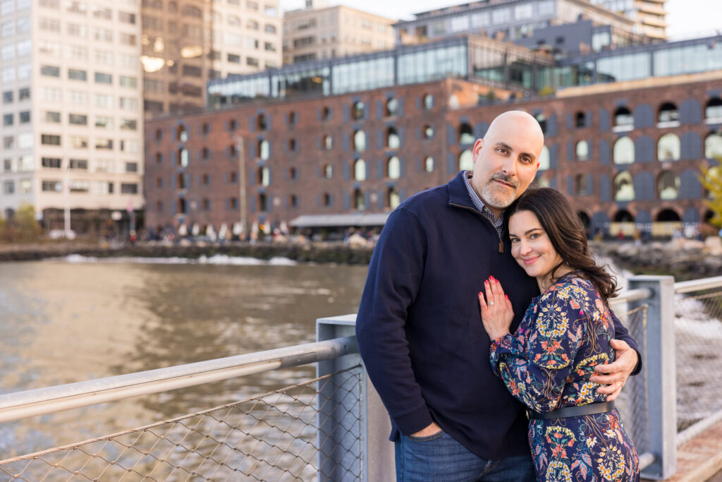 Winter engagement session NYC portrait of Regina and Dominick along the DUMBO waterfront, framed by brick warehouse facades and urban textures that define architectural engagement photos Brooklyn couples seek.