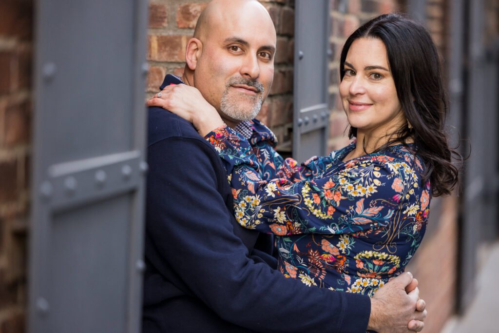 Architectural engagement photos Brooklyn featuring Regina and Dominick embracing between brick and iron textures in DUMBO, highlighting intimate winter engagement photos in DUMBO with refined urban composition.