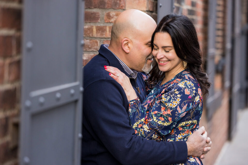 Capturing Regina and Dominick in an intimate embrace against classic brick facades and iron framing, emphasizing texture, connection, and refined urban engagement photos NYC style.