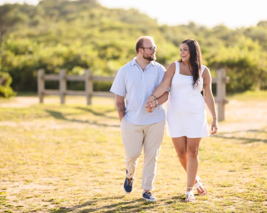 Engaged couple walking hand in hand during a Camp Hero engagement session in Montauk, NY, surrounded by sunlit fields and coastal landscape on the East End.