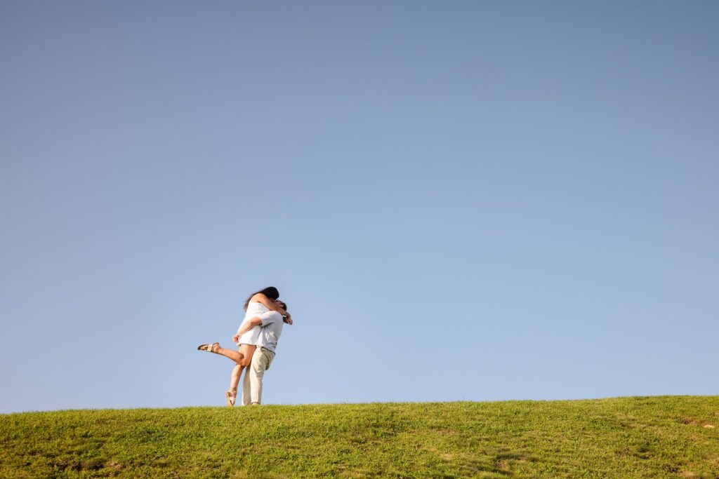 Couple embracing on a grassy bluff during a Montauk engagement session at Camp Hero State Park, framed against an open blue sky on the East End of Long Island.