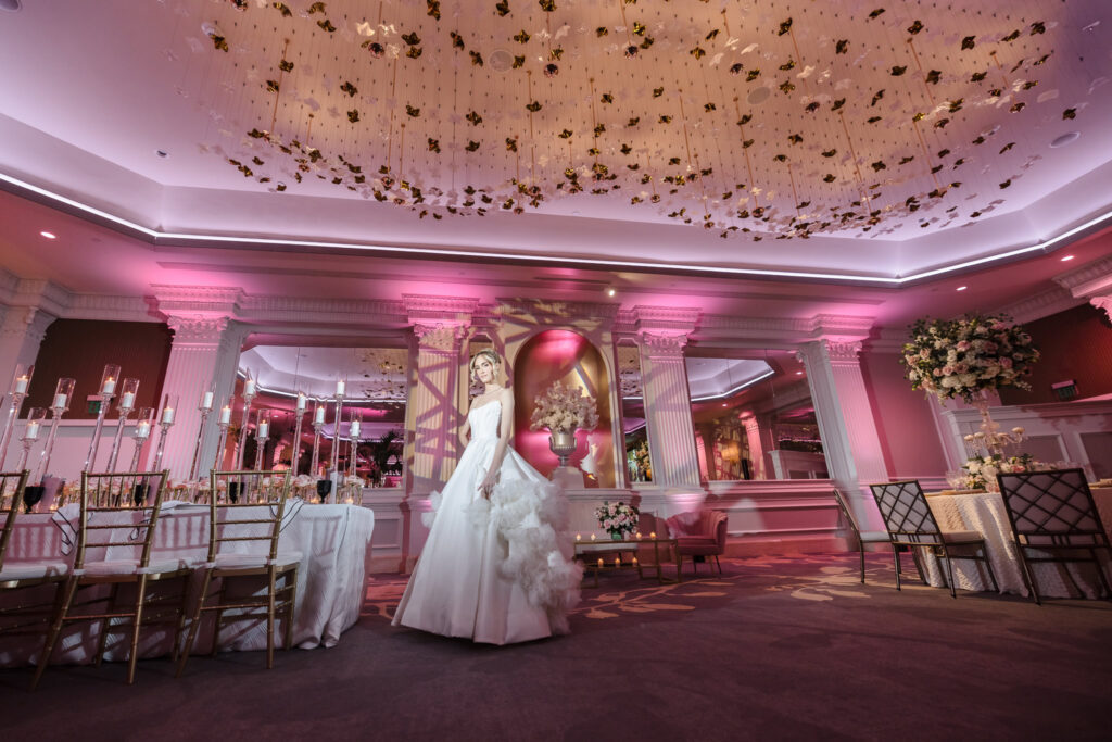 Wide view of the renovated Garden City Hotel ballroom with blush uplighting, sculptural ceiling installation, and bridal model during the Blush Hour wedding showcase in Garden City, NY.