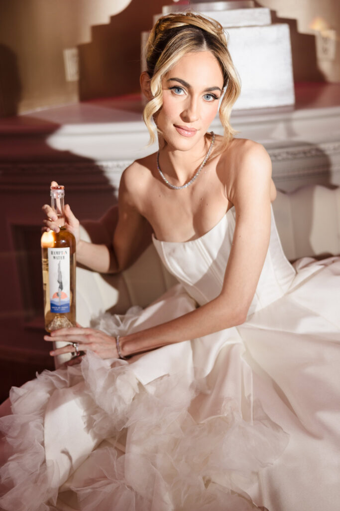 Bridal model in a strapless wedding gown holding a bottle of Hampton Water rosé during the Blush Hour showcase at the Garden City Hotel ballroom in Garden City, NY.