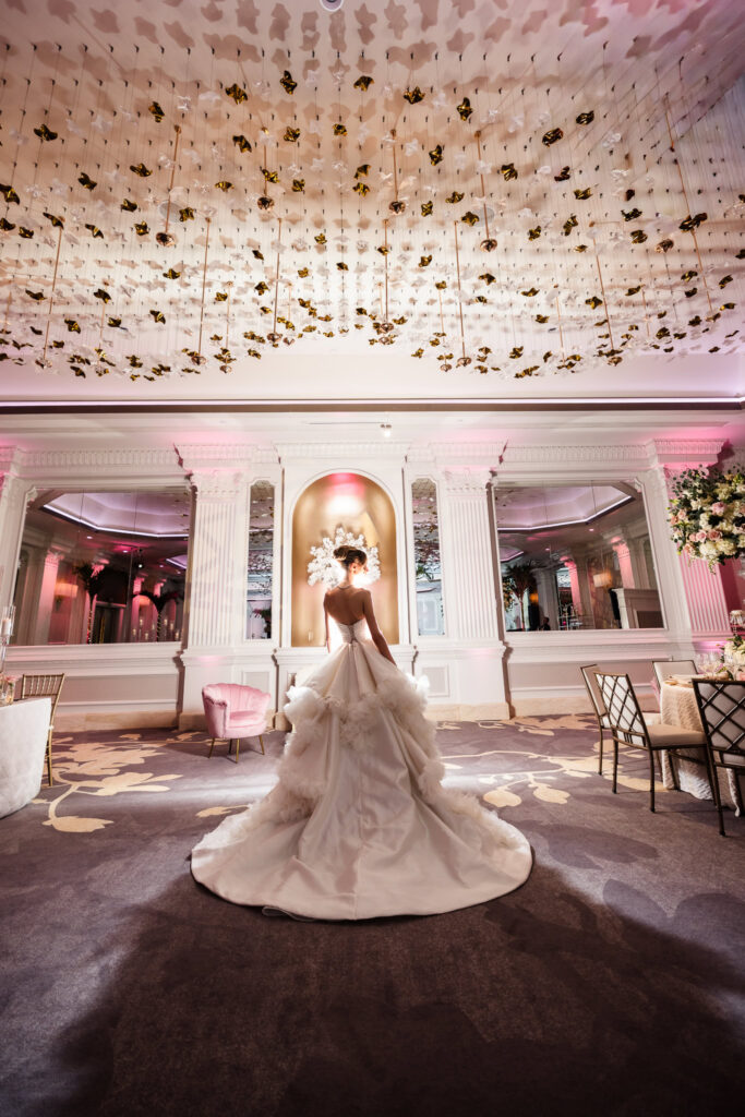 Bridal model in a dramatic wedding gown standing beneath the sculptural ceiling installation inside the Garden City Hotel ballroom, highlighting the elegant Long Island wedding venue during Blush Hour.