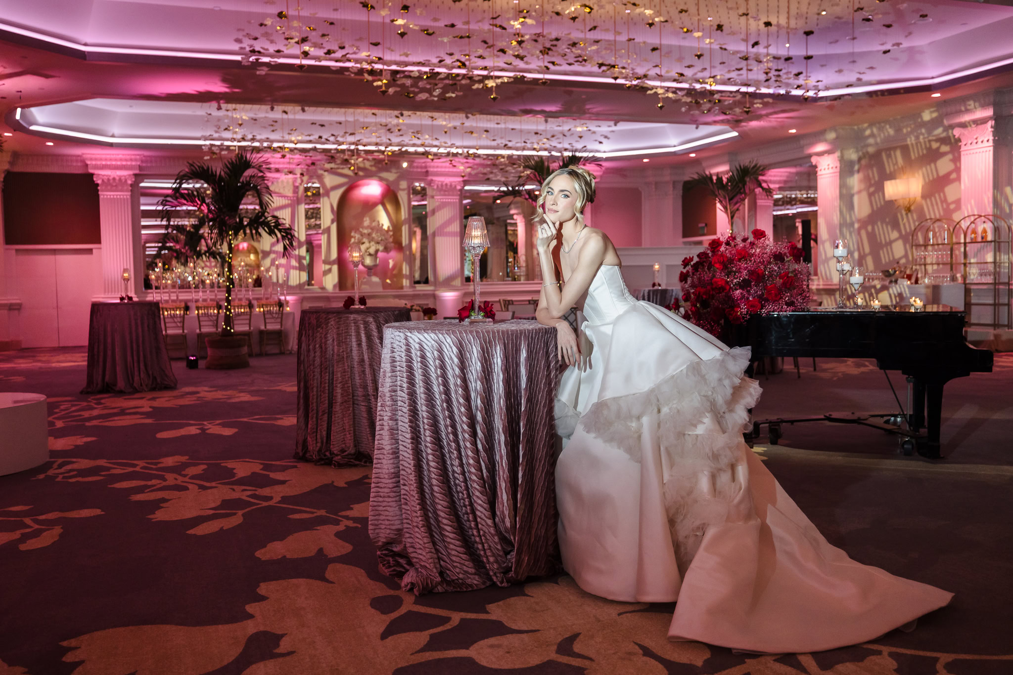 Bridal model in a strapless gown posing at a cocktail table beneath the sculptural ceiling installation inside the Garden City Hotel ballroom during the Blush Hour wedding showcase.