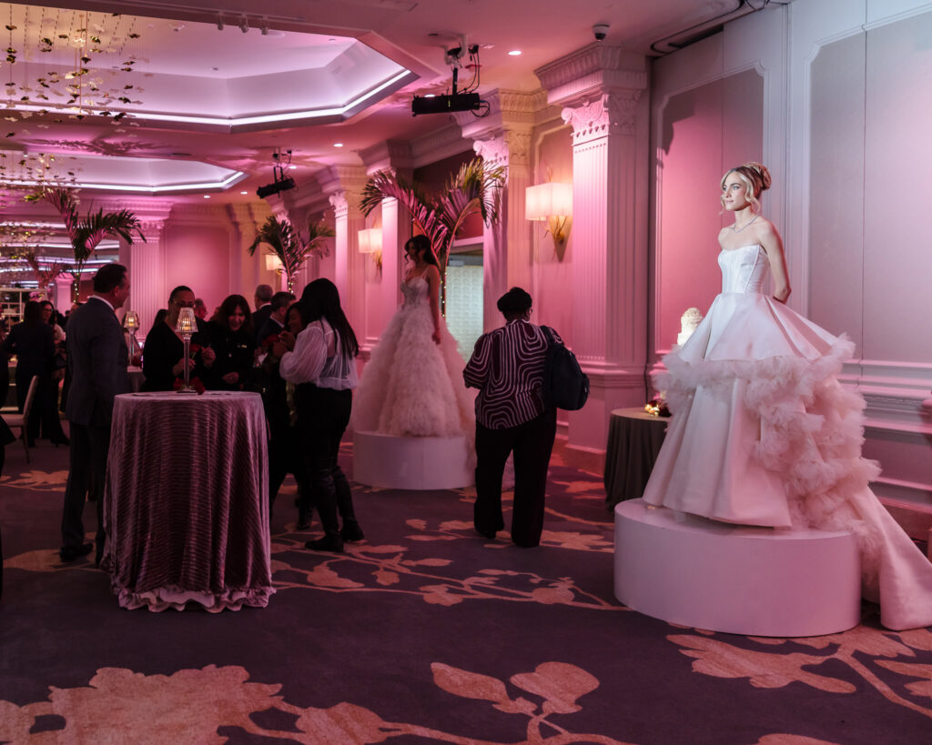 Guests mingling among cocktail tables while bridal gowns are displayed during the Blush Hour showcase inside the Garden City Hotel ballroom in Garden City, NY.