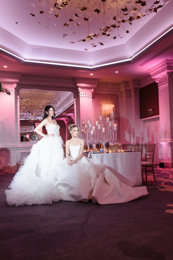 Bridal models in designer wedding gowns posed beside a romantic candlelit reception table beneath the sculptural ceiling installation inside the Garden City Hotel ballroom during the Blush Hour showcase.