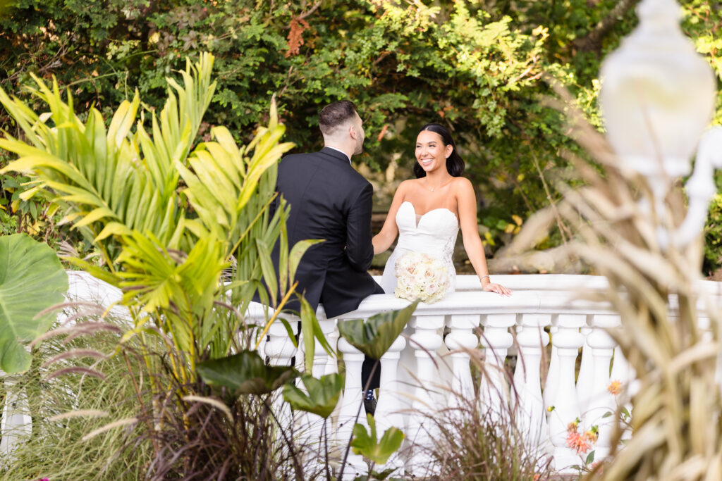 Romantic garden balcony portrait by a Luxury Wedding Photographer Long Island of a couple sharing a relaxed and joyful interaction