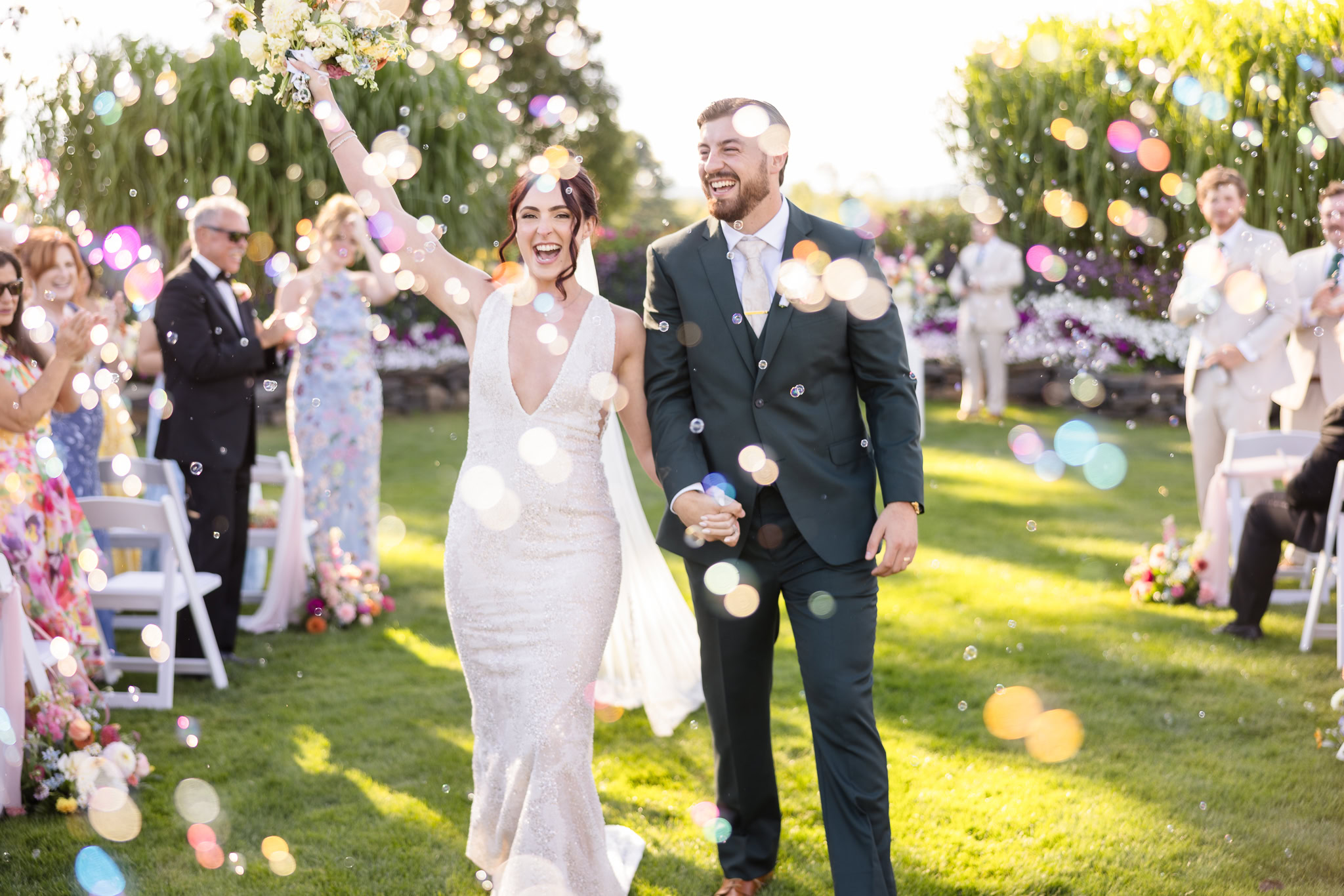Bride and groom walking down the aisle after their ceremony as guests toss bubbles, capturing a joyful and celebratory wedding moment outdoors