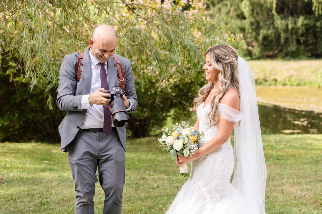 Wedding photographer showing a bride her portraits during an outdoor wedding portrait session beside a pond.