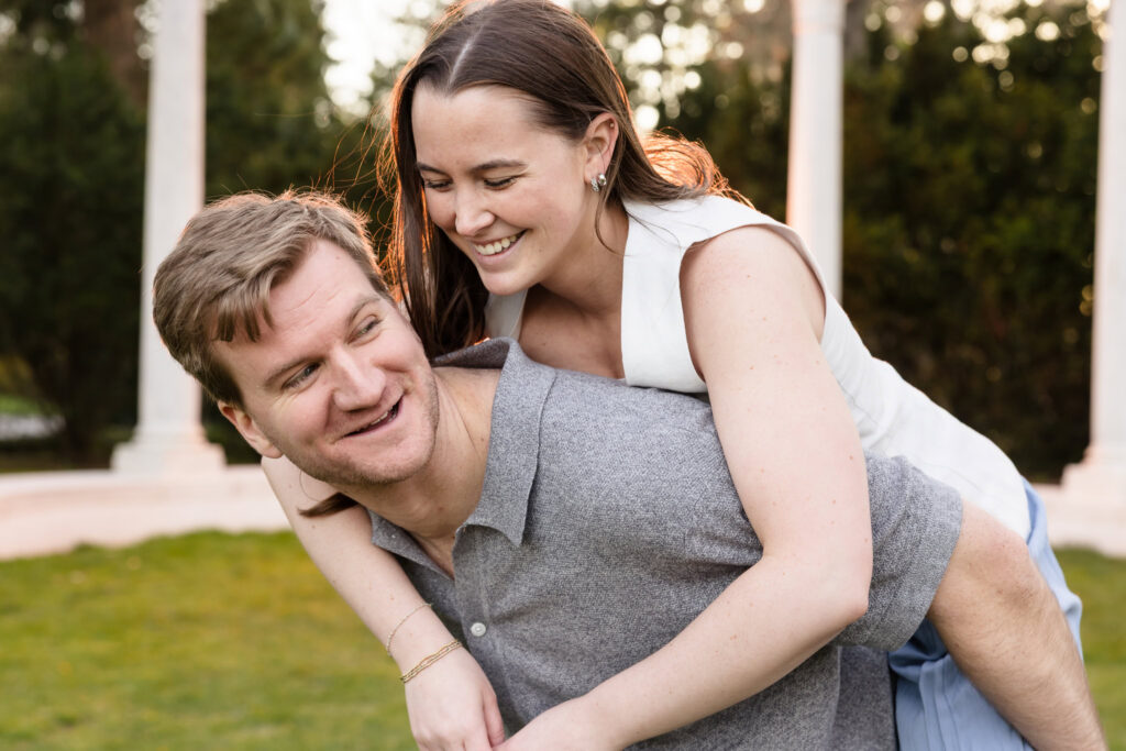 Joyful couple sharing a playful piggyback moment during an outdoor engagement session at sunset.