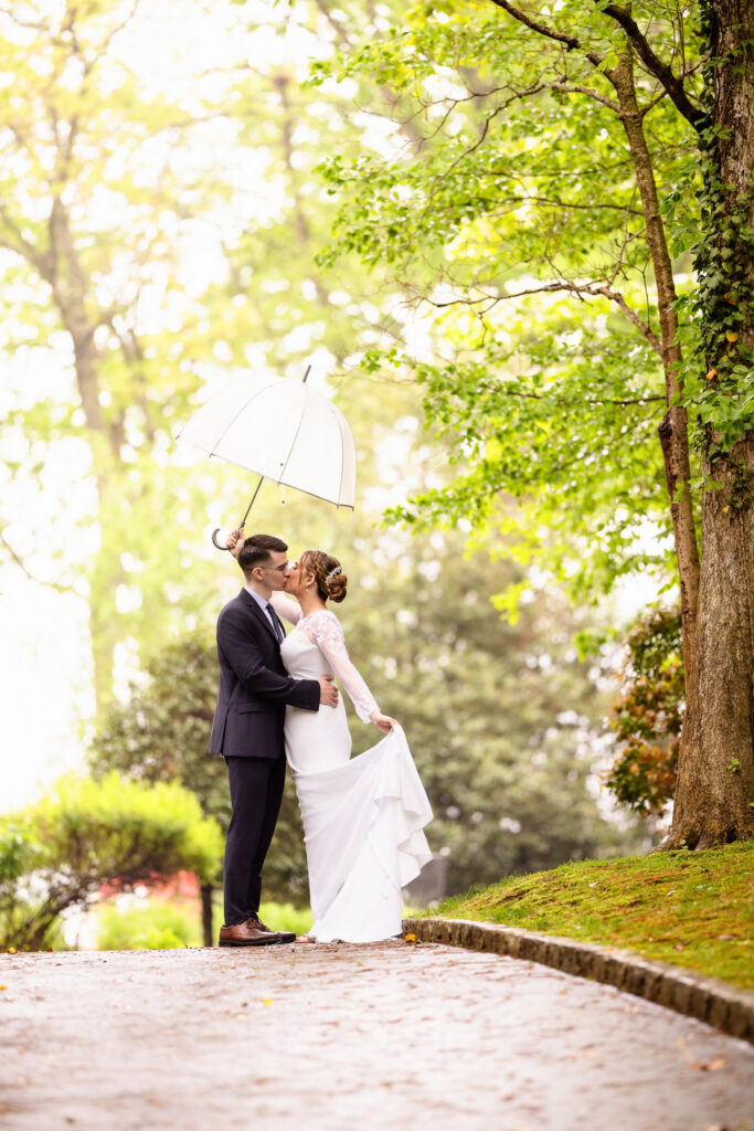 Couple sharing a kiss under an umbrella during a romantic rainy wedding portrait session on Long Island
