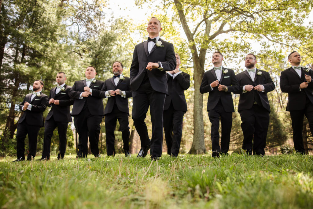 Groom and groomsmen standing outdoors in black tuxedos during a Long Island wedding portrait session.