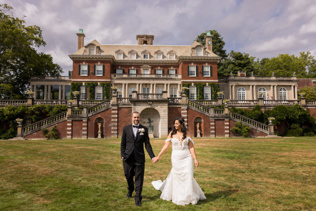 Bride and groom walking across the lawn in front of the historic Old Westbury Gardens estate on Long Island.