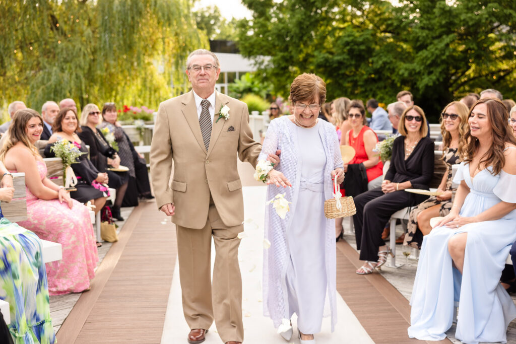 Grandparents walking down the aisle during an outdoor Long Island wedding ceremony surrounded by family and guests.