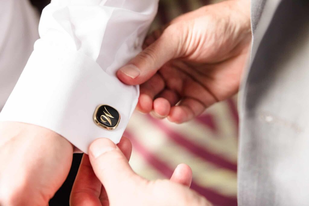 Close-up of a groom adjusting personalized cufflinks while getting ready on the wedding morning.