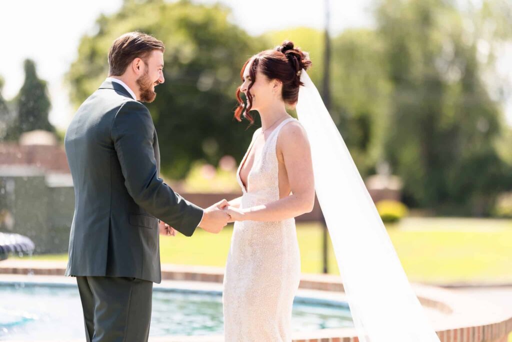 Bride and groom holding hands beside a fountain during an elegant outdoor wedding portrait session.