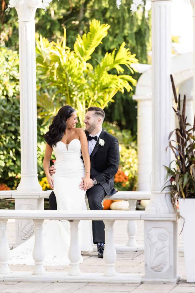 Bride and groom sharing a relaxed portrait beneath a white gazebo during a luxury Long Island wedding photography session.