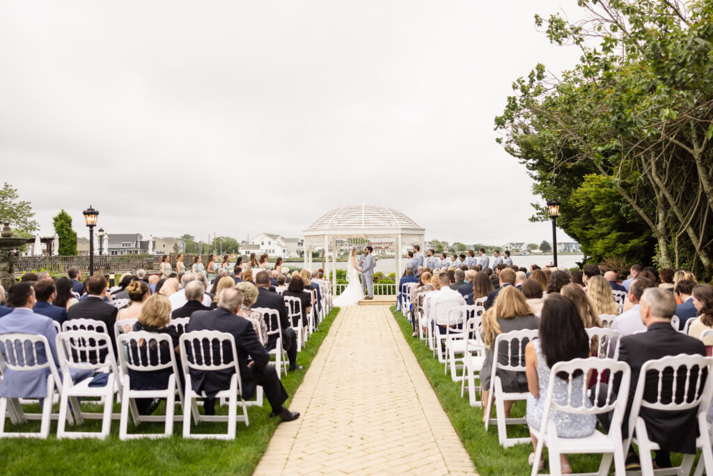 Outdoor waterfront ceremony setup at a Long Island wedding venue with white chairs and gazebo overlooking the water.