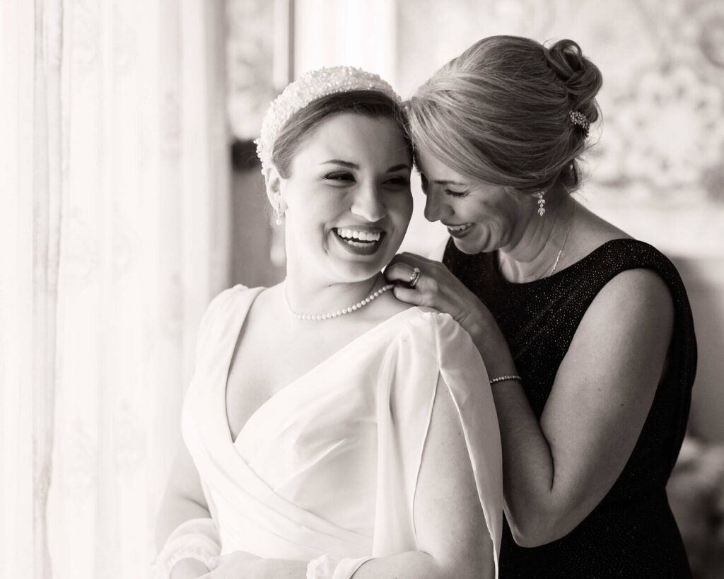 Mother fastening the bride’s necklace during a quiet getting ready moment by the window.