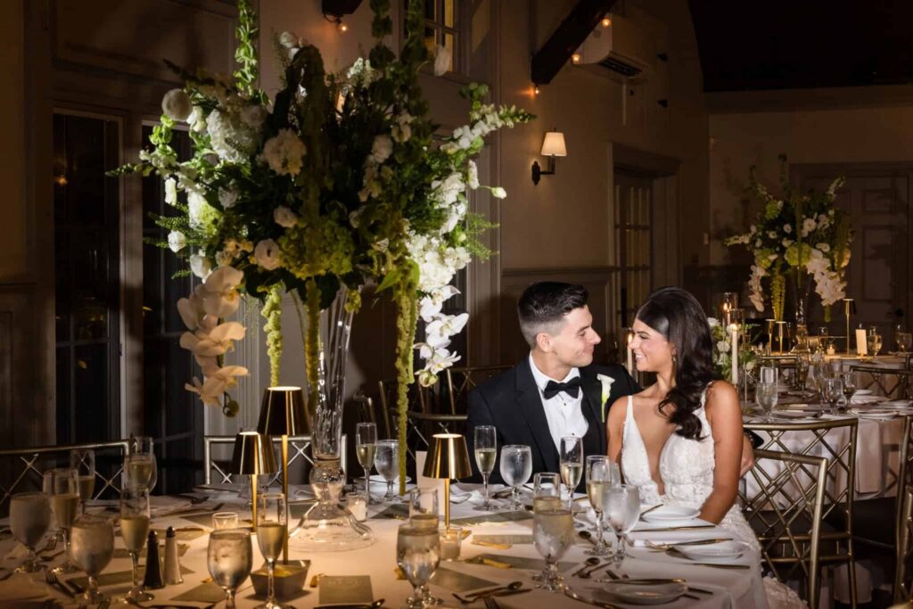 Bride and groom seated inside an elegant wedding reception space with luxury floral design and candlelight