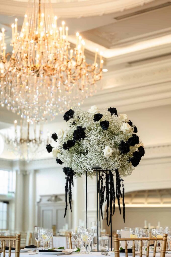 Tall floral centerpiece beneath chandeliers inside a luxury Long Island wedding venue ballroom reception space.
