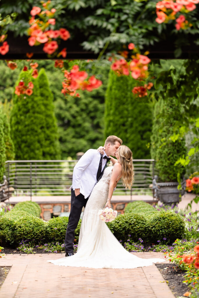 Bride and groom kissing in a lush garden setting at an elegant Long Island wedding venue with landscaped grounds and floral surroundings.