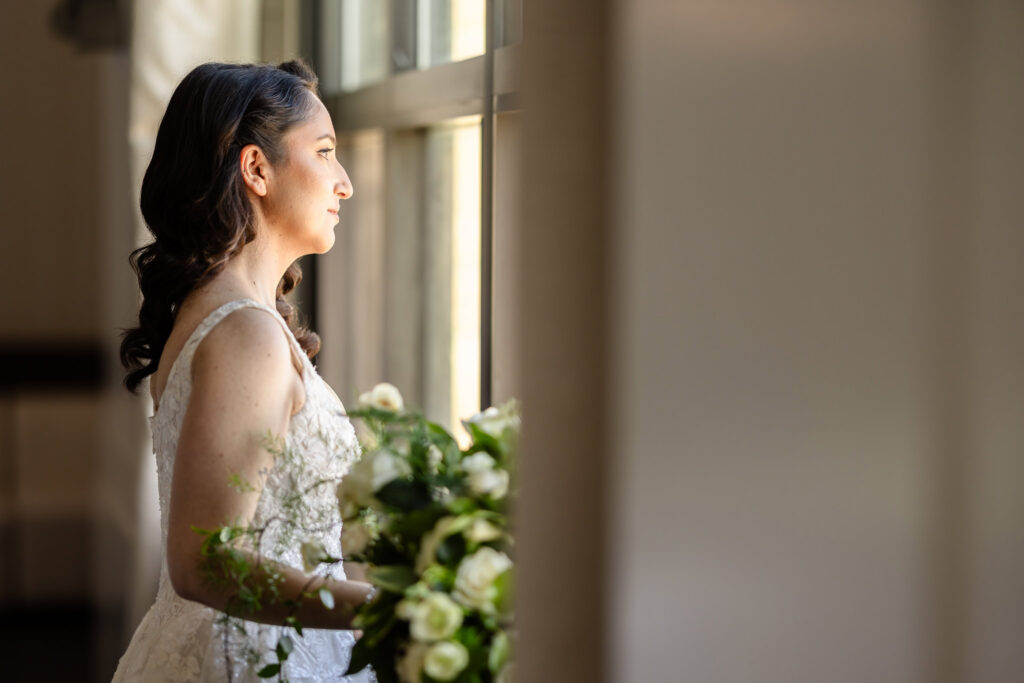 Bride gazing out a window while holding her bouquet during a 1920s wedding on Long Island.