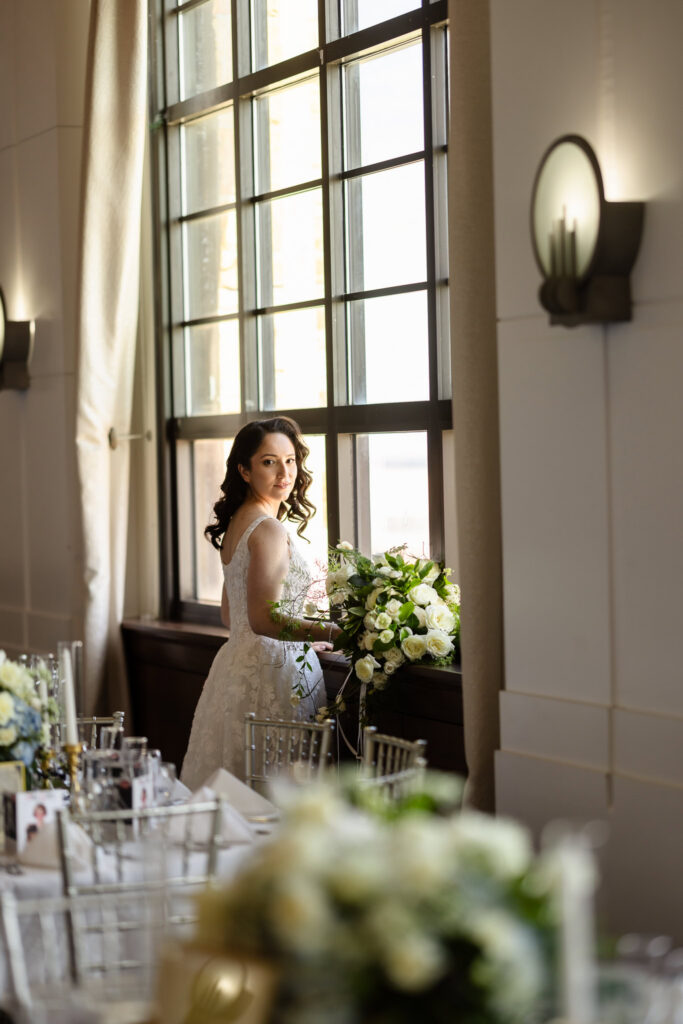 Bride holding a cascading white bouquet beside tall windows during a 1920s wedding Long Island celebration.