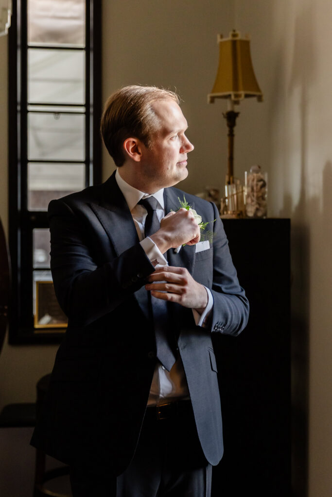 Groom adjusting his cufflinks in soft window light before a 1920s wedding Long Island ceremony.