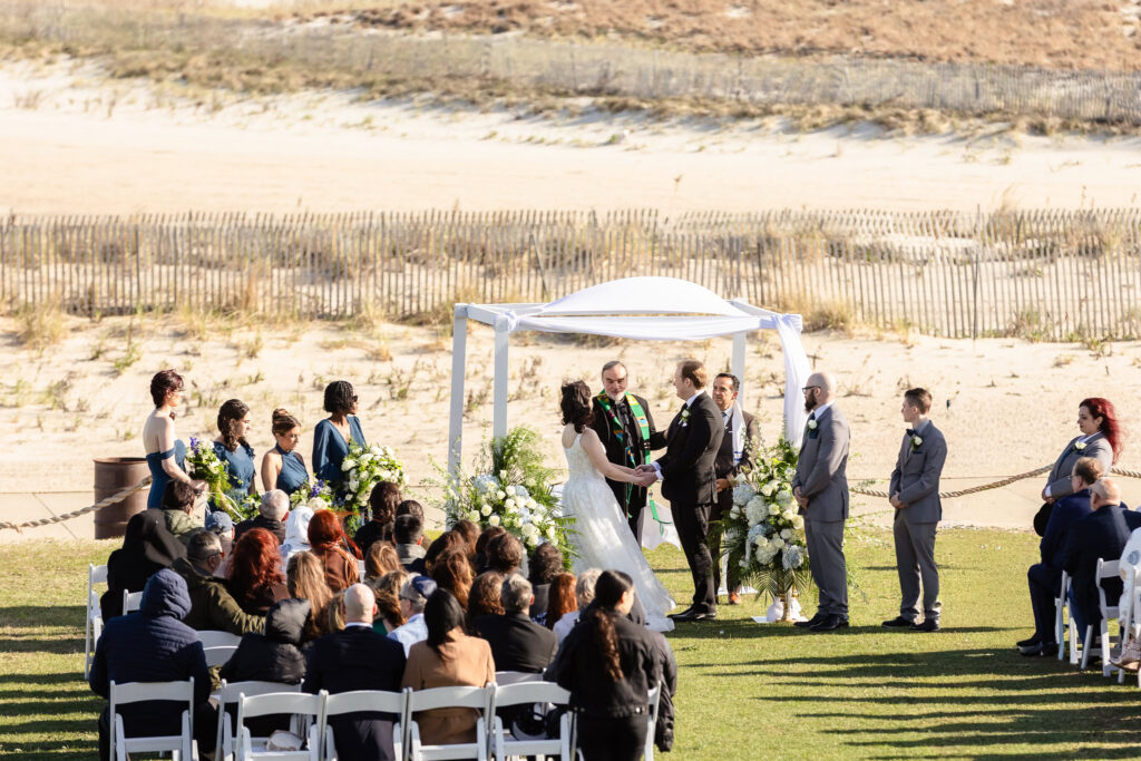 Couple exchanging vows beneath a white arbor at a 1920s wedding Long Island beachfront ceremony.