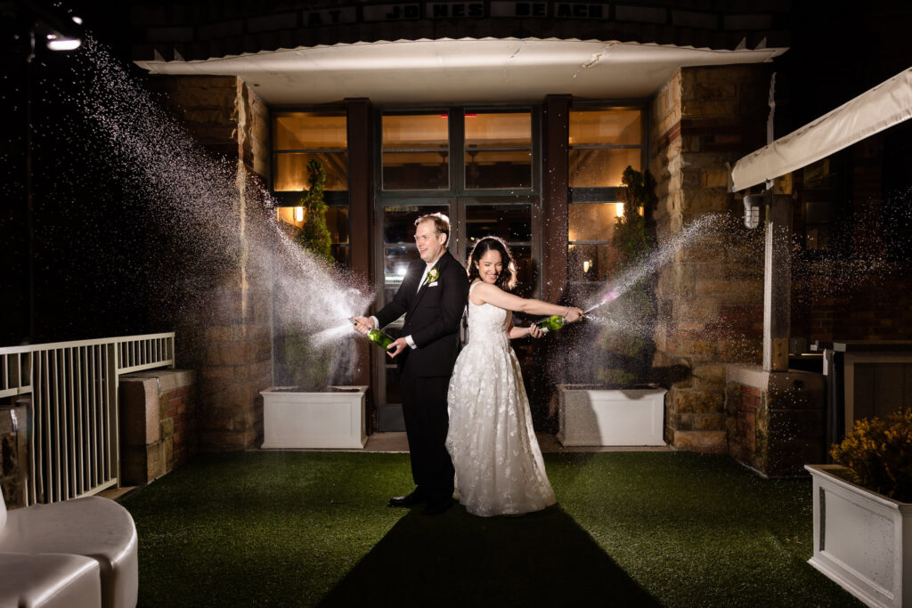 Bride and groom celebrating with a champagne spray outside the venue.