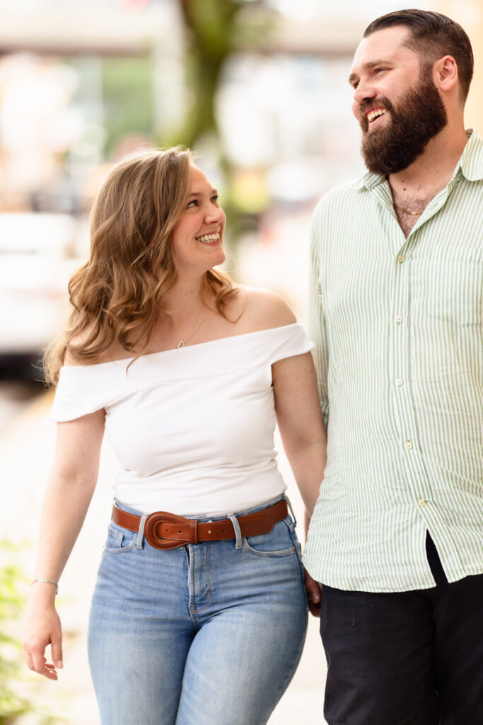 Engaged couple walking hand in hand through Long Island City while sharing a joyful moment.