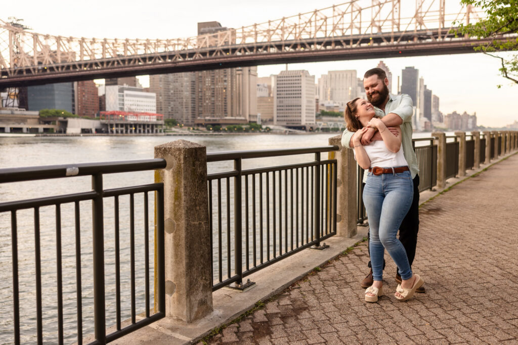 Couple laughing together beside the East River with the Ed Koch Queensboro Bridge spanning the background.