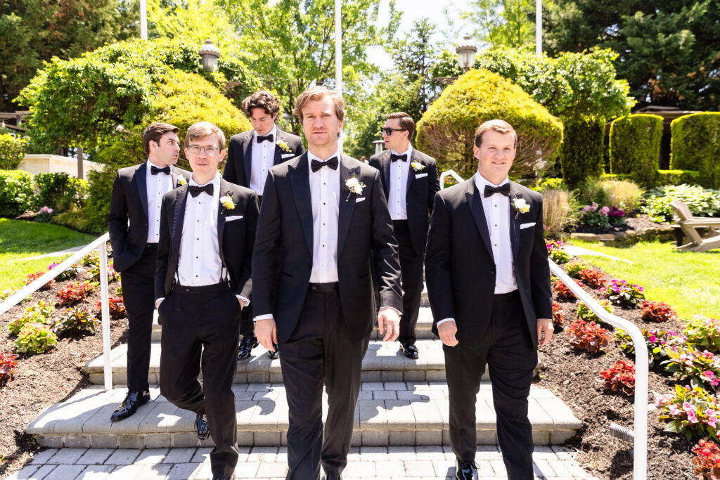 Kyle and his groomsmen walk through the gardens during portraits before Ashley and Kyle's Heritage Club wedding.