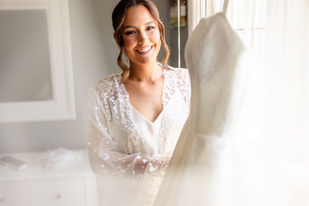 Ashley smiles beside her wedding dress while getting ready at her childhood home before her Heritage Club wedding.