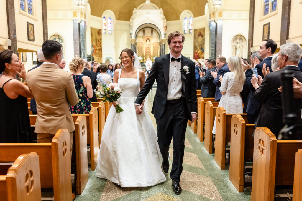 Ashley and Kyle walk down the aisle as newlyweds at St. Joseph's Church in Garden City while guests applaud.